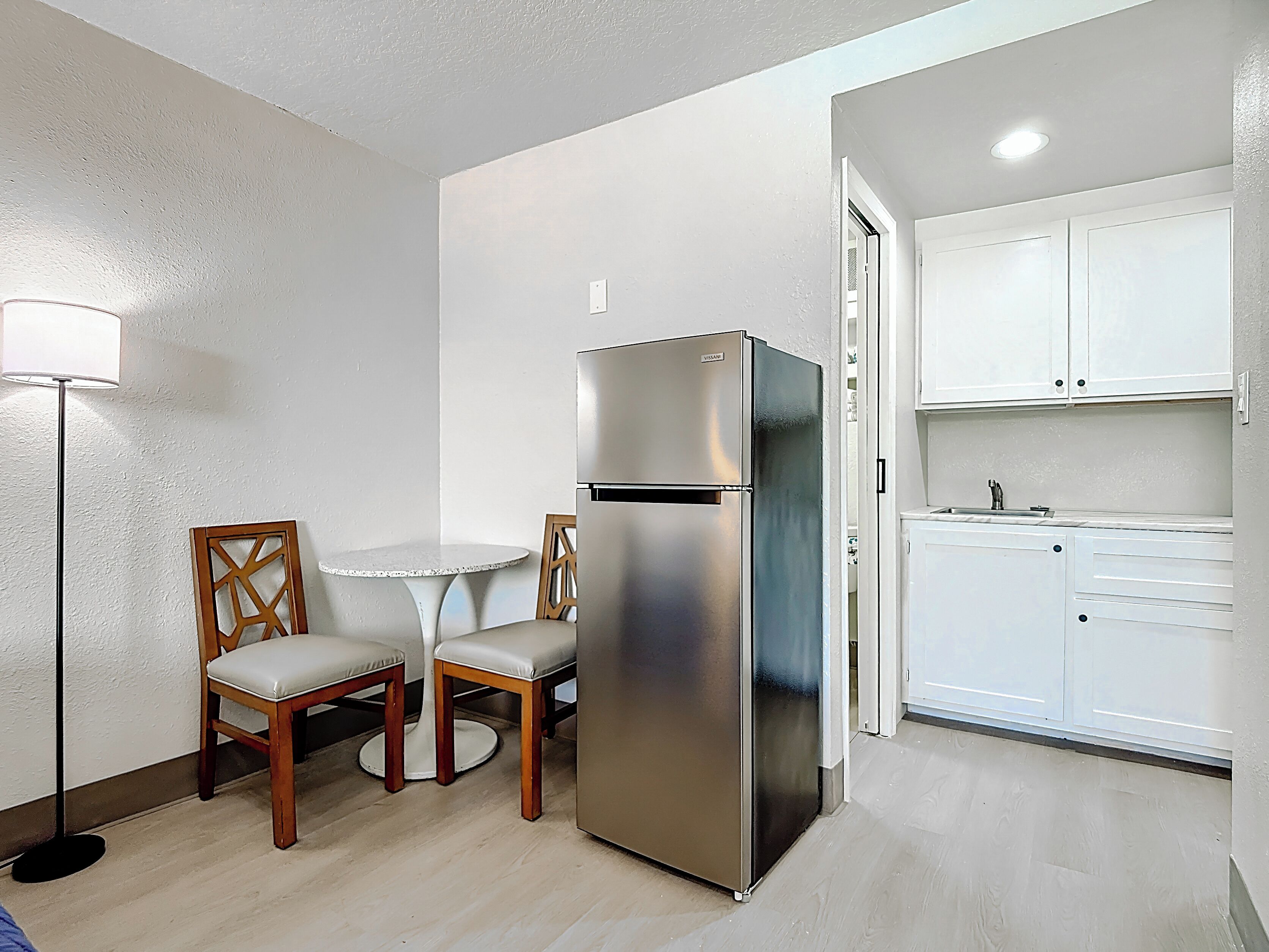 Una cocina compacta con refrigerador, una mesa de comedor con sillas y armarios blancos.