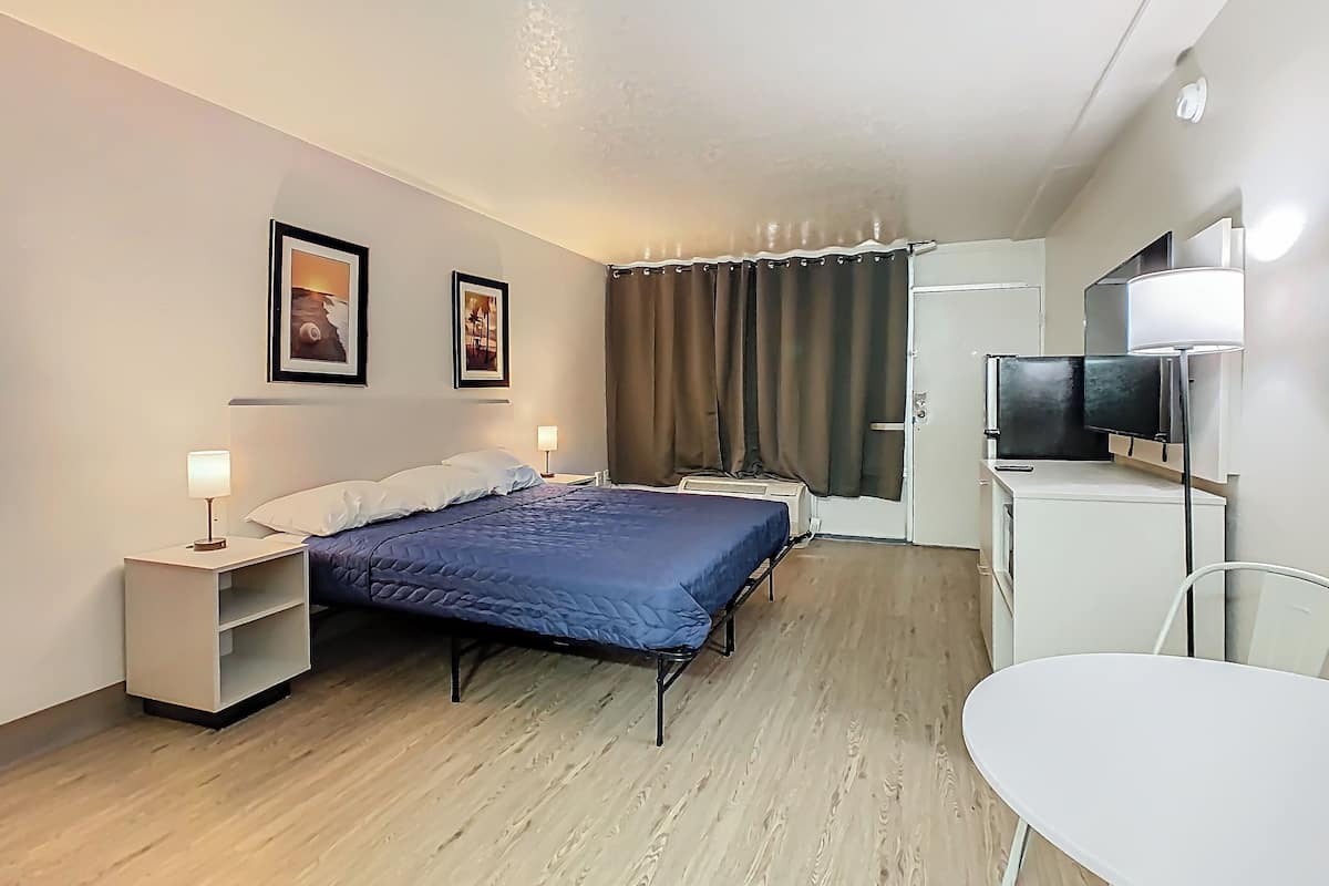 A hotel room with a bed, bedside tables, a TV, and a desk.