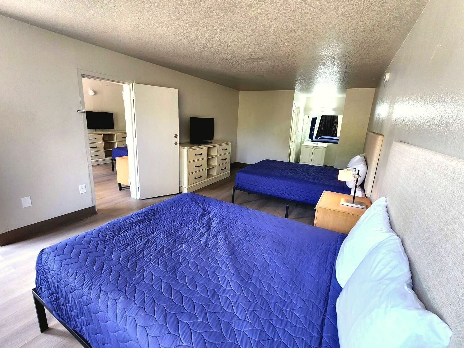A bedroom with two beds, a dresser, a television, and a mirror.