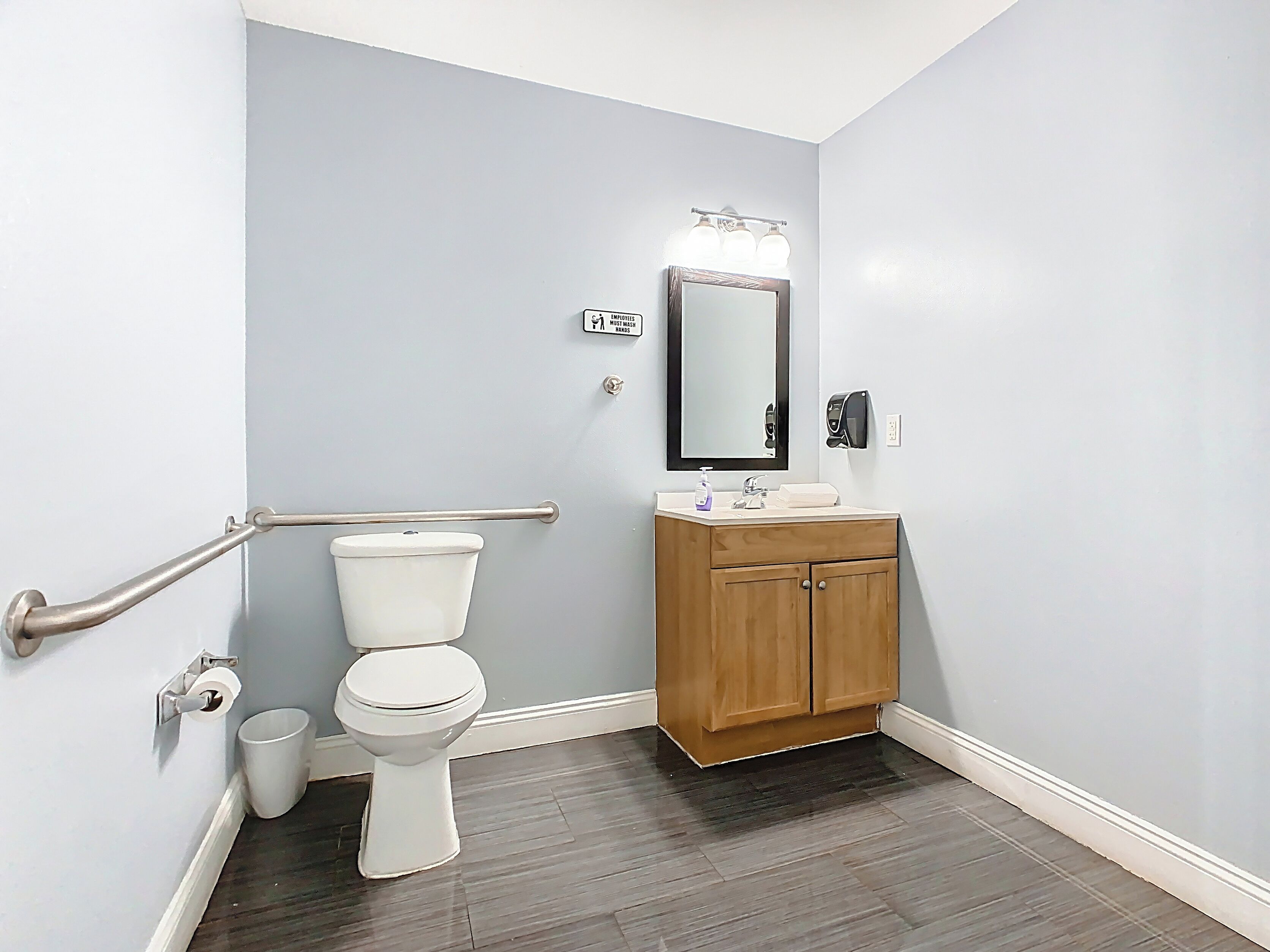 A bathroom with a toilet, a wooden cabinet, a mirror, and a hand sanitizer dispenser.