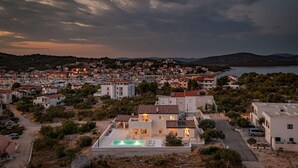 Un quartier résidentiel en bord de mer, avec une maison imposante dotée d’une piscine, entourée d’autres maisons et d’une marina en arrière-plan.