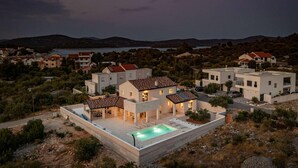 Une villa moderne dotée d’une piscine, entourée d’un paysage vallonné et bordée, au loin, par une étendue d’eau.