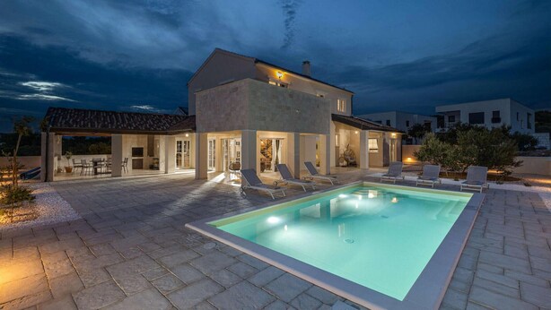 Une maison moderne dotée d’une piscine, d’un espace salon extérieur et d’un patio couvert.