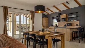 Une cuisine moderne avec un îlot central en bois, des chaises noires et une table à manger agrémentée d’une bouteille et de verres.