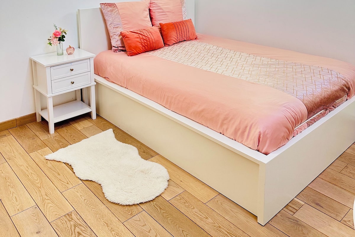 A bedroom with a bed, nightstand, and a white rug.