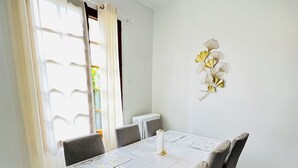 A dining area with a table set for six, white walls, and a radiator on the wall. - JABEEN'S HOUSE (Bezons)
