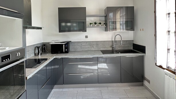A modern kitchen with stainless steel appliances, a built-in microwave, and a large window providing natural light. - JABEEN'S HOUSE (Bezons)