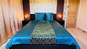 A bedroom with a large bed, a geometric-patterned bedspread, a textured wall, and a wooden door. - JABEEN'S HOUSE (Bezons)