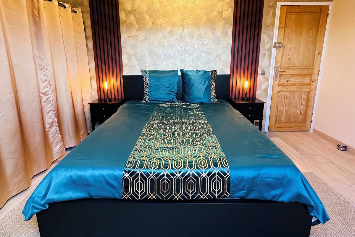 A bedroom with a large bed, a geometric-patterned bedspread, a textured wall, and a wooden door.