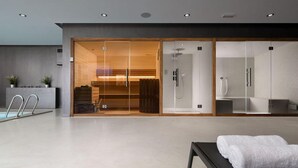 Una moderna spa con sauna in vetro, zona doccia separata e panca con asciugamani.
