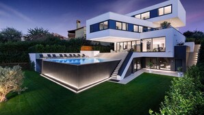 Una moderna casa a due piani con una grande piscina, area salotto esterna e una scala che conduce al piano superiore.
