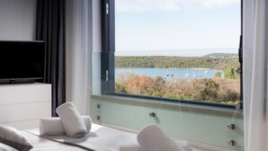 Una camera da letto con un letto, una TV fissata al muro e una finestra vista su un corpo d'acqua e vegetazione.