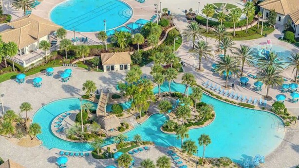 Eine Vogelperspektive zeigt einen luxuriösen Rückzugsort mit mehreren Schwimmbecken, Palmen und Liegestühlen.