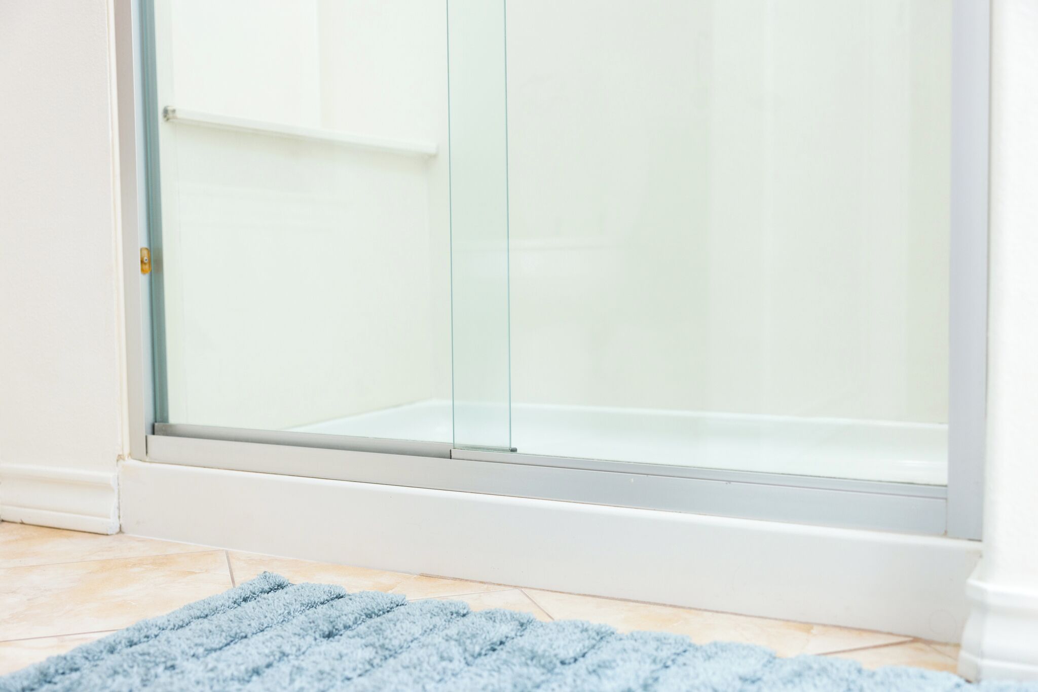 A bathroom with a glass shower enclosure and a blue rug on the floor.