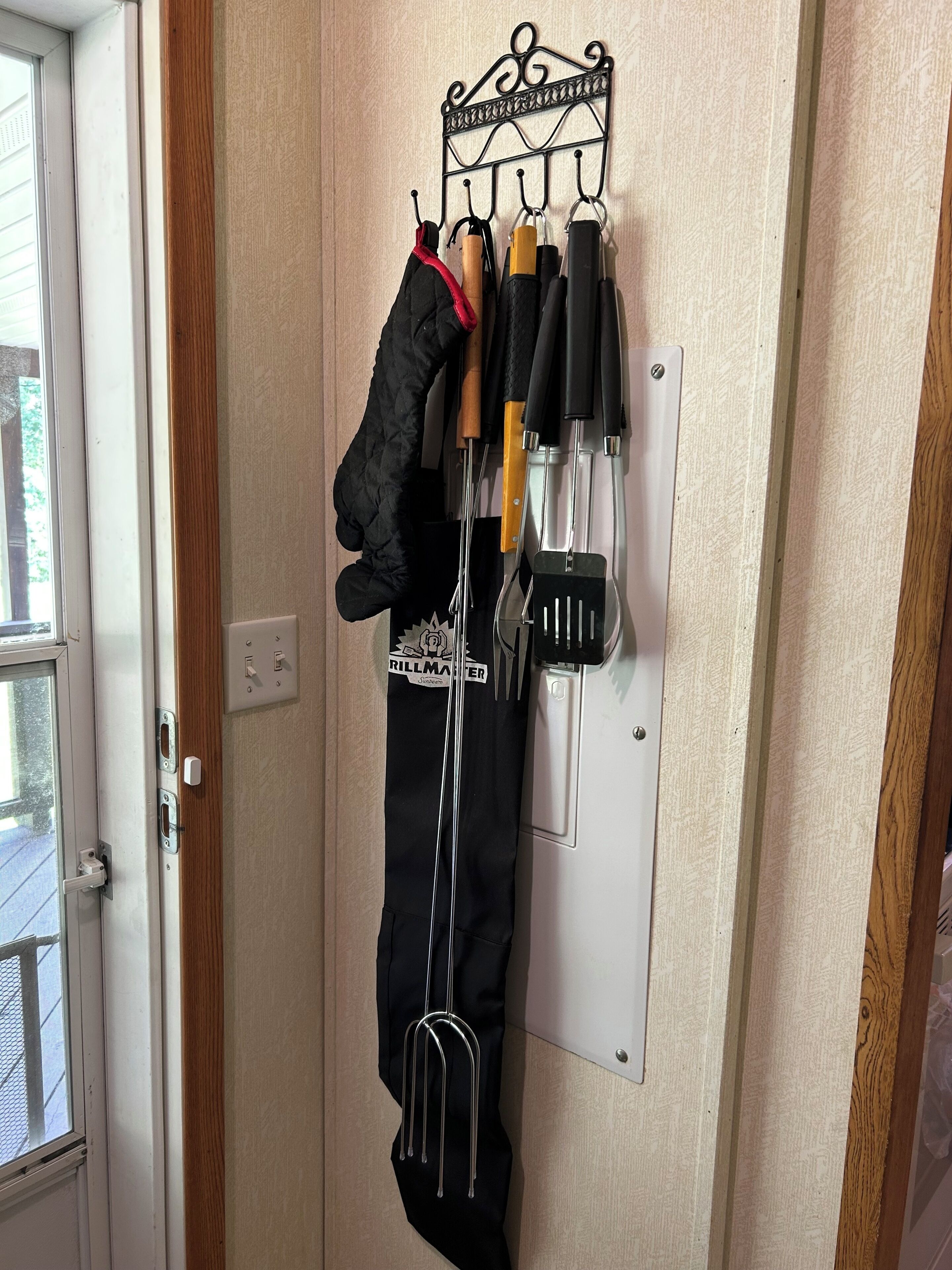 Un crochet fixé au mur, sur lequel sont suspendus divers ustensiles de cuisine, et un tablier noir est accroché en dessous.