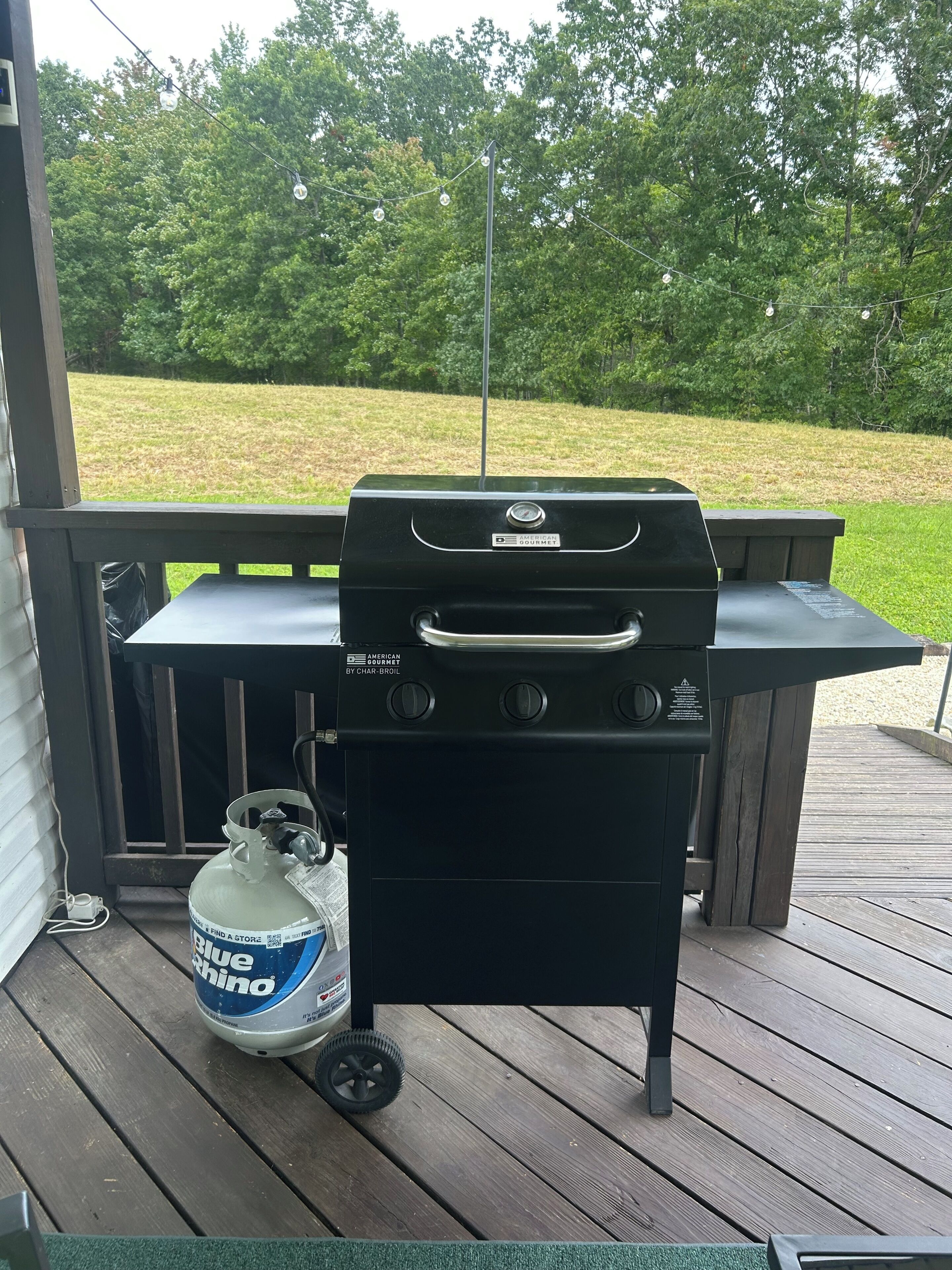 Ein Grill auf einer Holzterrasse mit einem Propangasbehälter in der Nähe.