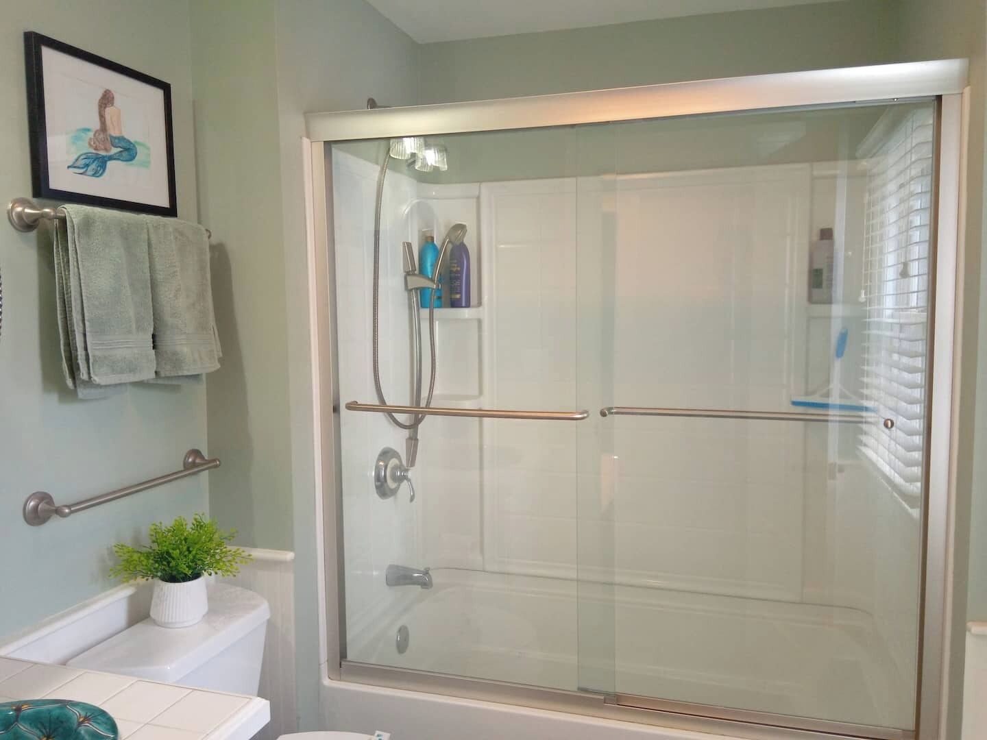 A bathroom with a glass-enclosed shower, a toilet, a sink, and a framed picture on the wall.