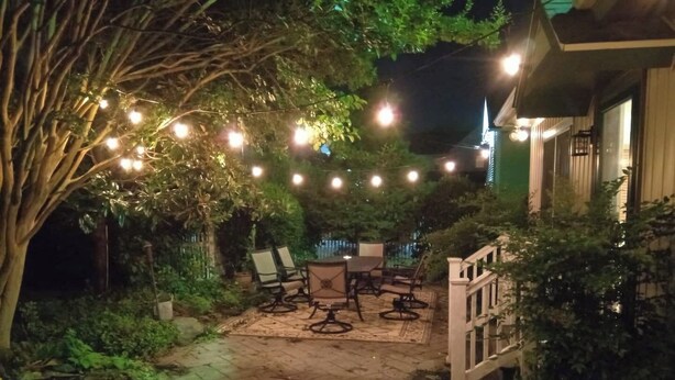 En udendørs patio med en sti af sten, et bord med stole og lyskæder.