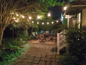 An outdoor patio area with a stone pathway, a table with chairs, and string lights.