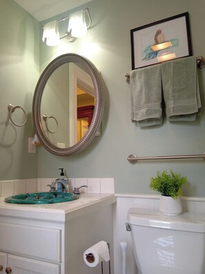 A bathroom with a large mirror, a sink with a decorative tray, a toilet, and a towel rack with towels.