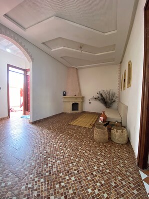 A spacious room with a tiled floor, a fireplace, and a large window.