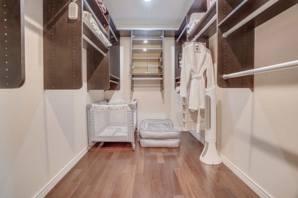 A narrow walk-in closet with built-in shelves, a radiator, a baby crib, and a standing fan.