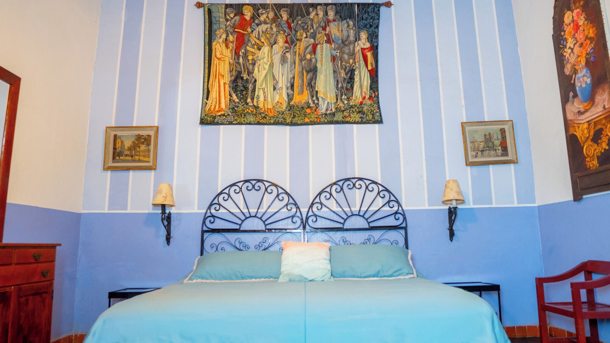 Un dormitorio con una cama, dos lámparas de pared y un tapiz en la pared.
