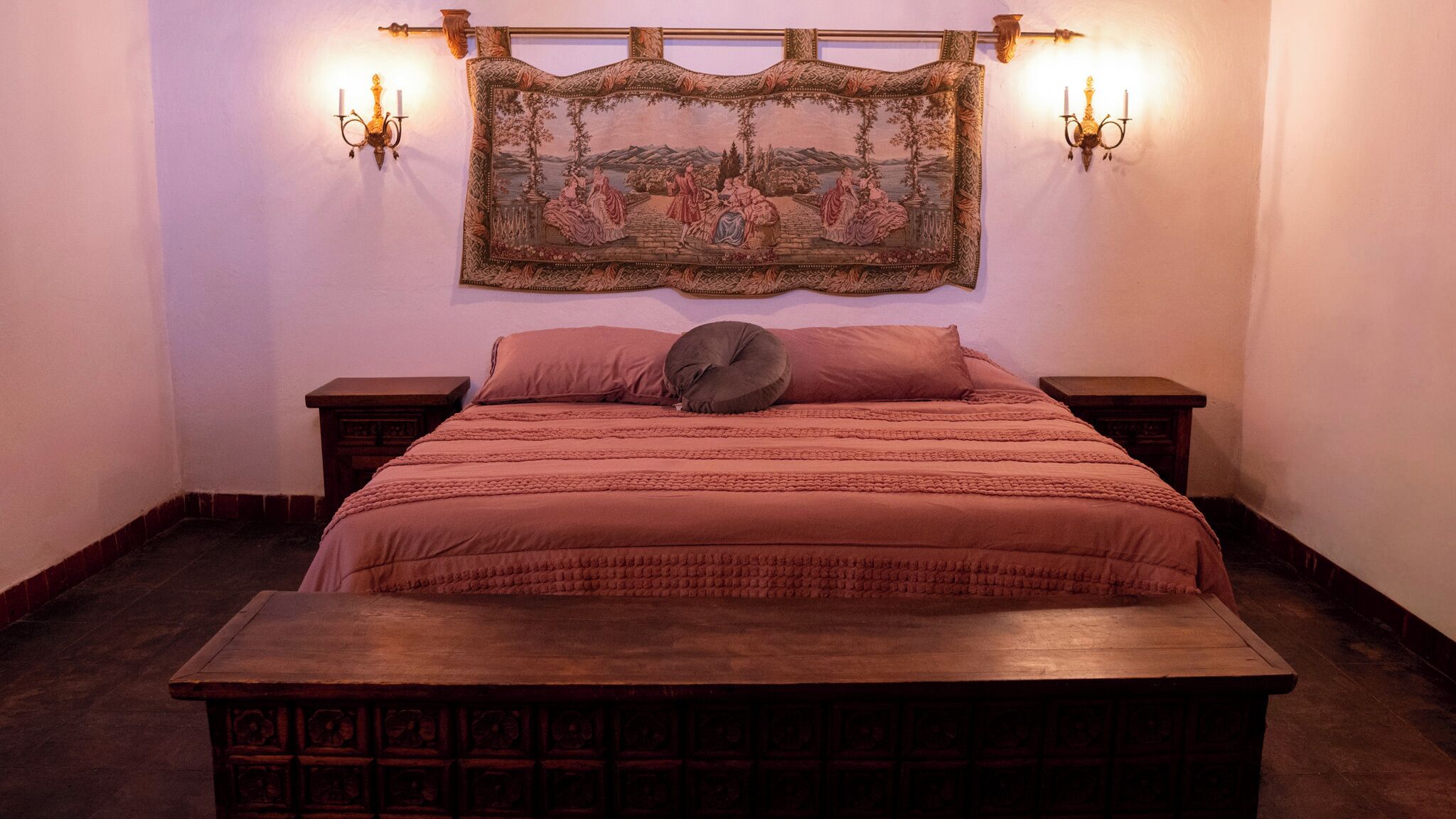 Un dormitorio con una cama grande, dos mesitas de noche, un banco de madera y un tapiz en la pared.