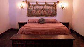 Un dormitorio con una cama grande, dos mesitas de noche, un banco de madera y un tapiz en la pared.