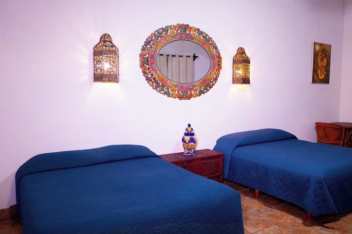 Una habitación con dos camas, un espejo e iluminación en la pared.