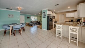 Uma cozinha espaçosa com armários brancos, uma área de jantar com mesa e cadeiras, e uma sala de estar com sofá e mesa de centro.