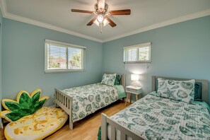 Un dormitorio con dos camas individuales, un ventilador de techo y dos ventanas con persianas.