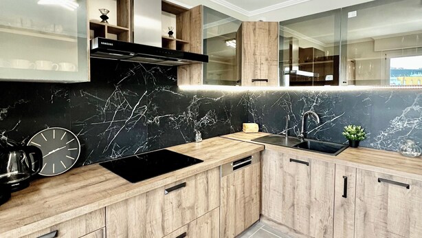 A modern kitchen with wooden cabinets, a black countertop, and a marble backsplash.