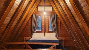 A cozy attic bedroom with a wooden sloped ceiling, a bed with white linens, and a small table. - Villa Park Chalés  (Penha)