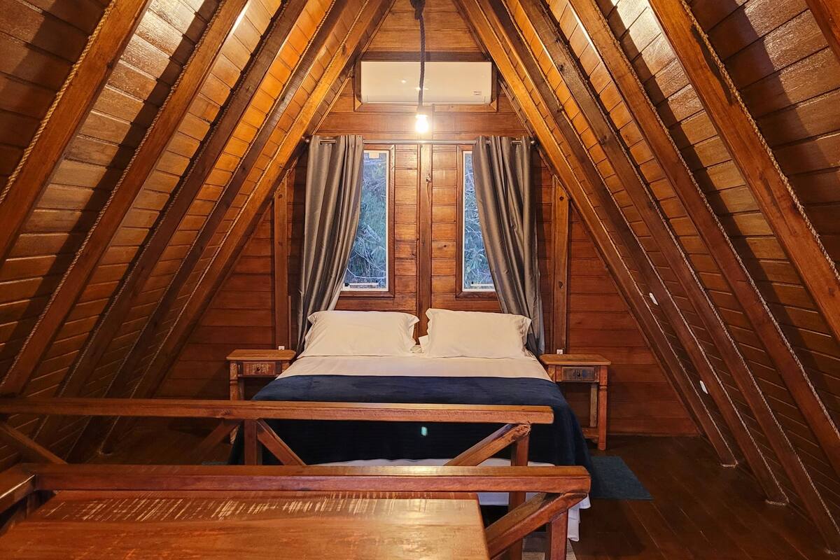Un dormitorio acogedor en el ático con techo inclinado de madera, una cama con sábanas blancas y una pequeña mesa.
