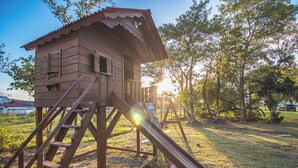 A wooden playhouse with a slide, surrounded by trees and grass. - Villa Park Chalés  (Penha)