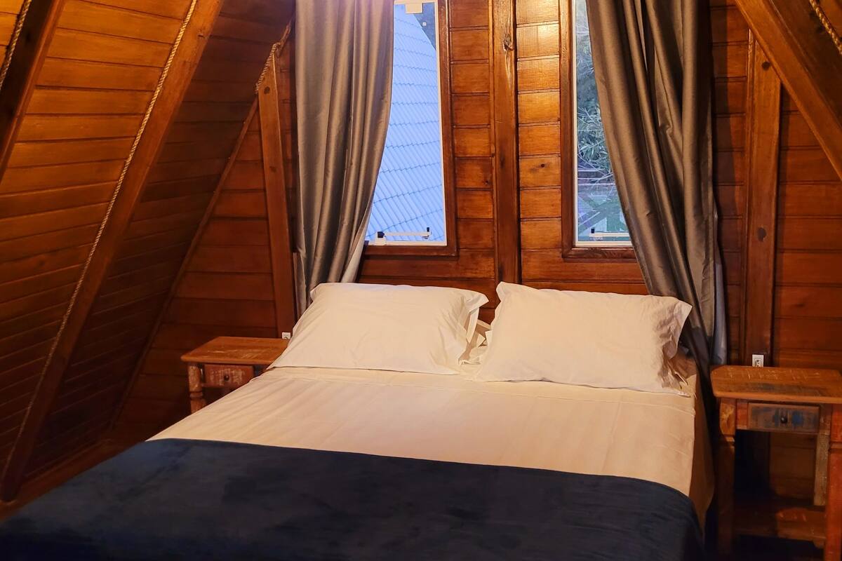 Una habitación acogedora con paneles de madera, una cama, dos mesitas de noche y un ventanal con cortinas.