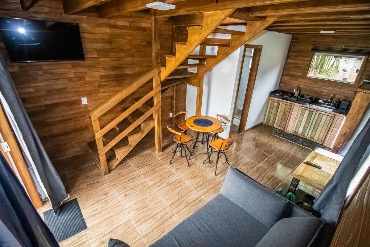 Un interior de madera con una escalera, un comedor con una mesa redonda y sillas, una zona de cocina y un sofá.
