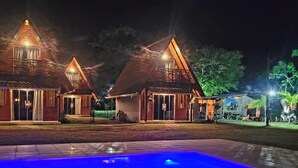 A nighttime view of a resort with three wooden cabins and a swimming pool. - Villa Park Chalés  (Penha)