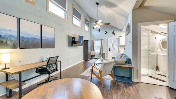 A modern living room with a wooden dining table, a sofa, a TV mounted on the wall, and a ceiling fan. - Old Forge Studio: Close to Lakes & Hiking Trails (Old Forge)