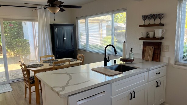 A modern kitchen with a central island, a ceiling fan, and a view of the outdoors. - Cozy townhome with backyard retreat! Minutes to wineries and downtown. (Livermore)