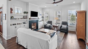Amplia sala de estar con chimenea, un sofá, dos sillones, un televisor y un mueble de madera.
