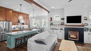 Una cocina moderna con armarios de madera, una isla central y un comedor con sofá blanco y taburetes de madera.