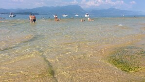 Een strand met helder ondiep water, boten en bergen op de achtergrond.
