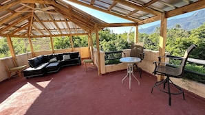 En overdækket terrasse med en sort modulsofa, et rundt bord og to stole.