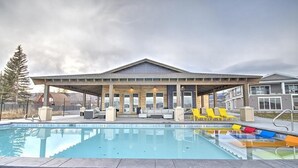 A covered outdoor swimming pool with lounge chairs and a building with large windows in the background.