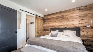 A bedroom with a bed, a bench, wooden wall paneling, and a door.