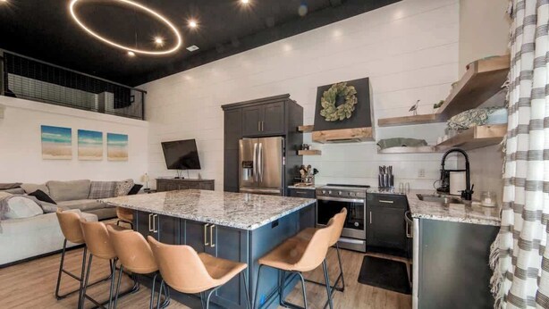 A modern kitchen with a central island, bar stools, a refrigerator, and a stove.