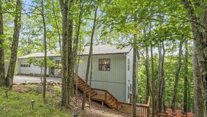 Une cabane avec un escalier en bois menant à une terrasse, le tout entouré de grands arbres.