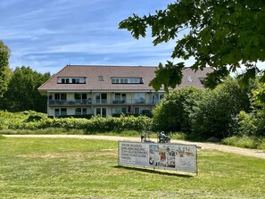 A two-story building with a tiled roof, surrounded by greenery and a grassy area. - 3002 - Grömitz - Wohnung 3002 am Schoor in Grömitz (Grömitz)